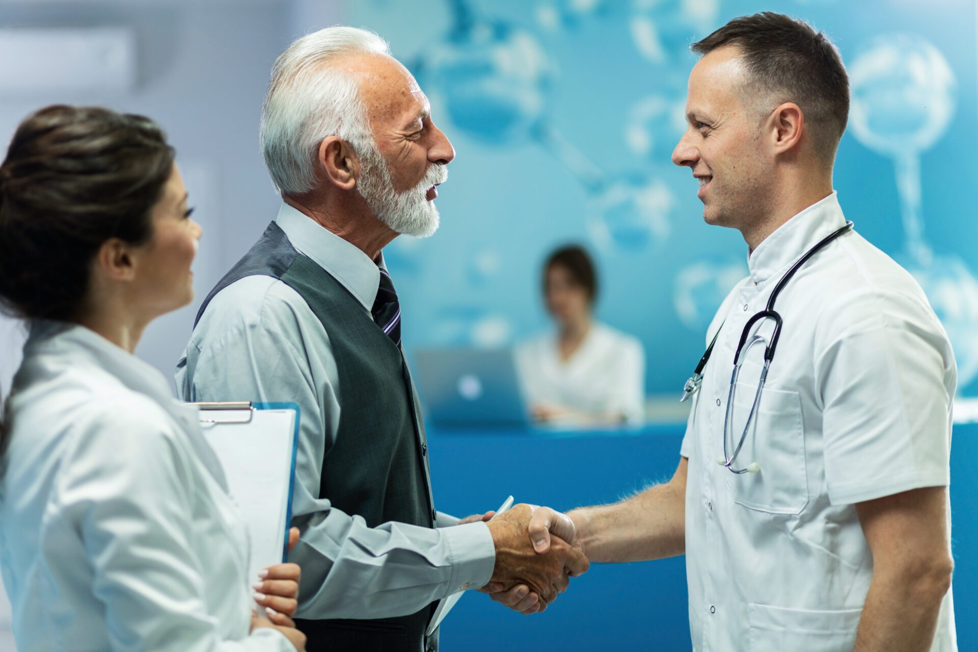 Happy senior man and male doctor handshaking while greeting in a hallway at clinic.
